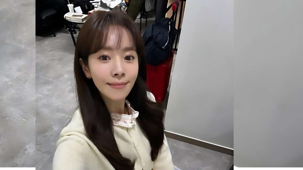 Han Ji-min with long dark hair in a cream knit sweater, posing for a selfie in a modern studio with gray floors.