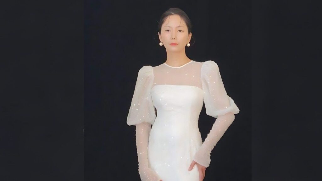 Hwang In-young stands against a dark backdrop in a white, sparkling gown with sheer puff sleeves and pearl earrings.