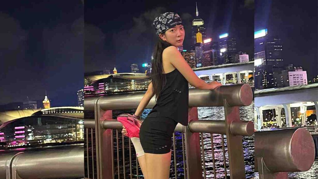 Jo Ayoung in black tank top and shorts leans on a metal railing, bandana and pink sneakers, lights behind.