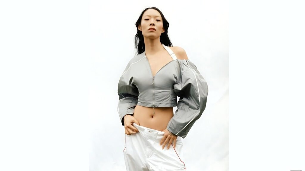 Josette Pimenta model poses against a light backdrop in a silver cropped top with front zipper and puff sleeves, exposing her midriff and white pants.