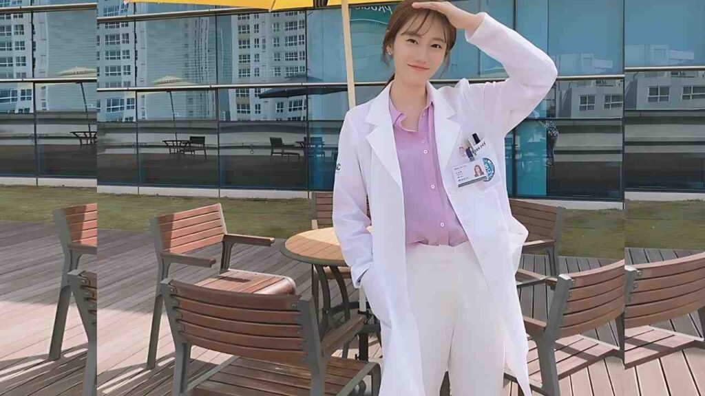 Jung Min-ah in a white lab coat over a pink blouse stands on a patio, shielding her eyes with one hand near a round table.