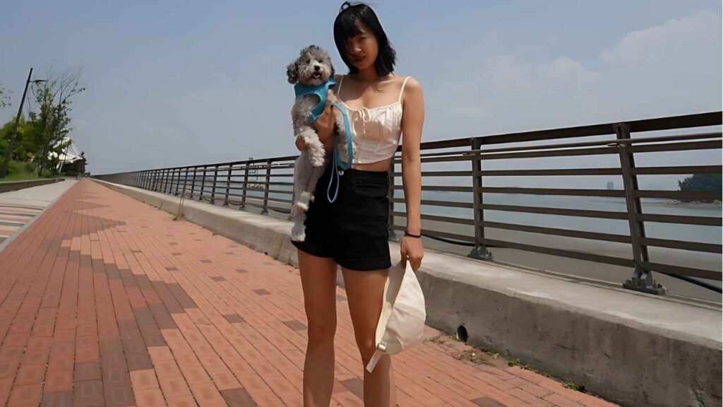 Jung Min-gyul in a short skirt stands on a sidewalk, holding a small dog close to her side.