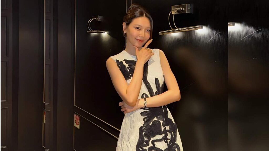 Jung Soo-young in a sleeveless white dress with bold black print poses in a sleek, dim, black-walled hallway; chin on her hand.