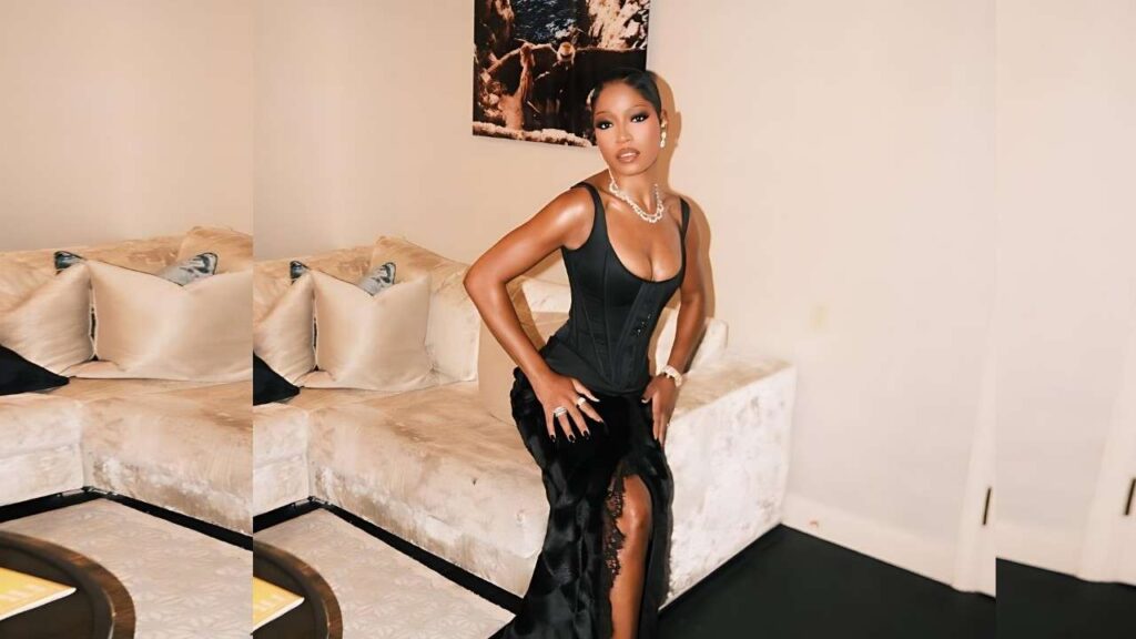 Keke Palmer in a black corset top and floor-length slit skirt poses in a beige living room with a cream sofa.