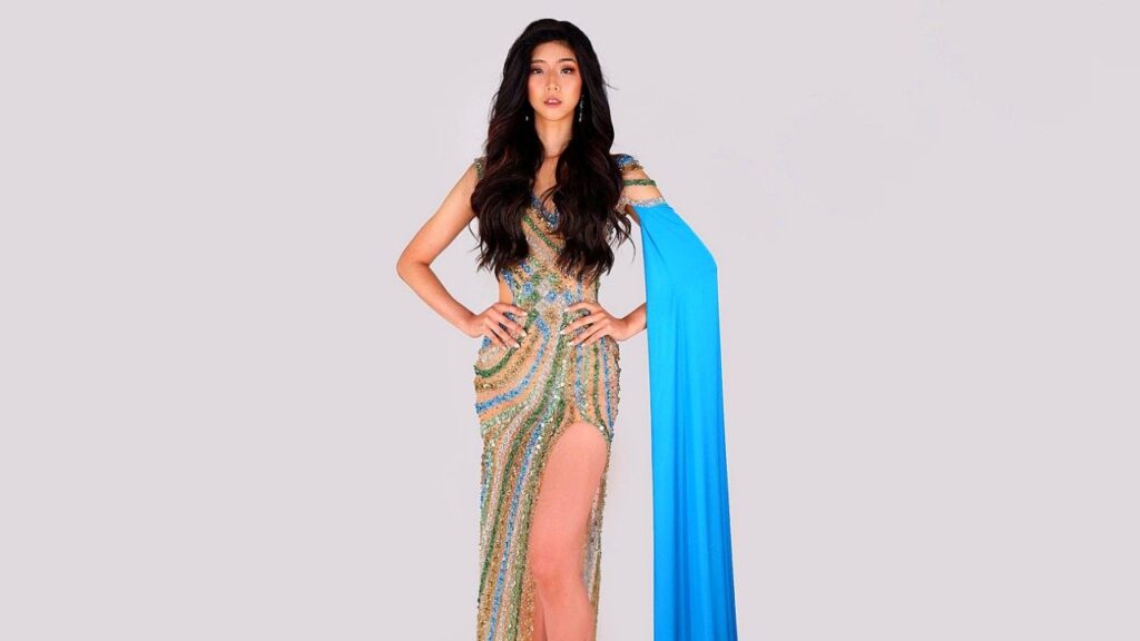 Kim Ho-jung stands with hands on hips in a sparkling gold-silver sequined gown with a high slit and blue cape.