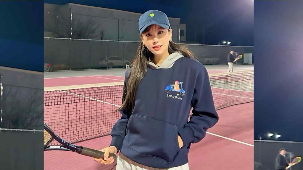 Kim Joo-ri in navy Bellus Buddy hoodie and cap holds a racket, net and another blurred player in background.