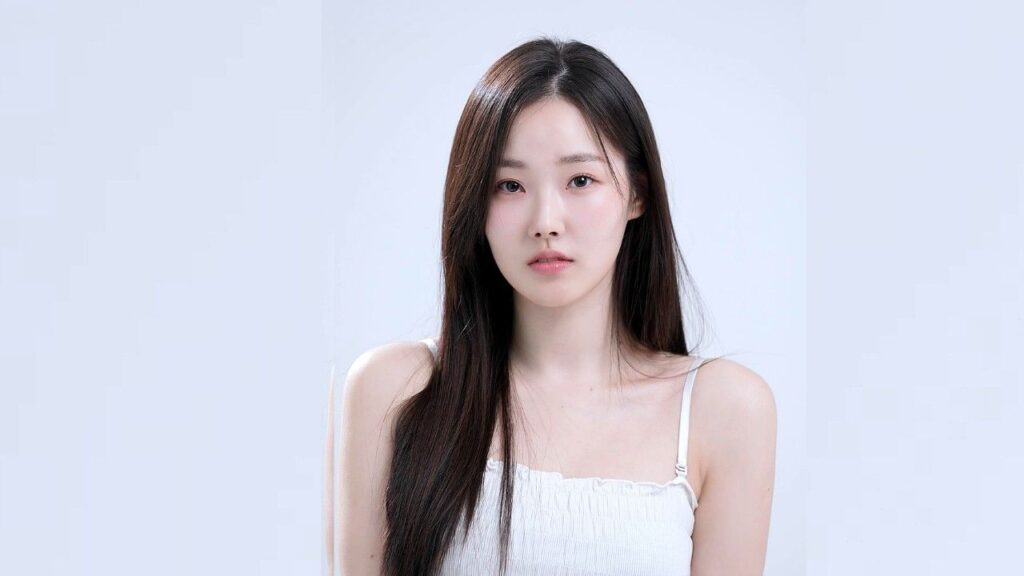 Kim Ju-eun with long dark hair in a white spaghetti-strap top, standing before a pale backdrop with a neutral expression.
