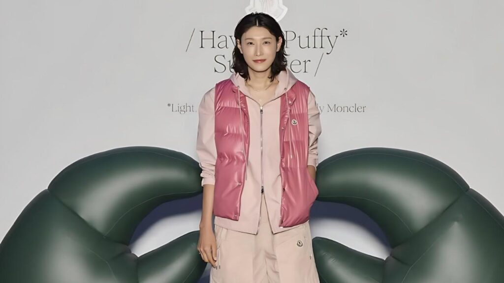 Kim Yeon koung in a pink puffer vest over a light pink hoodie and cargo pants poses between oversized green inflatable loops.