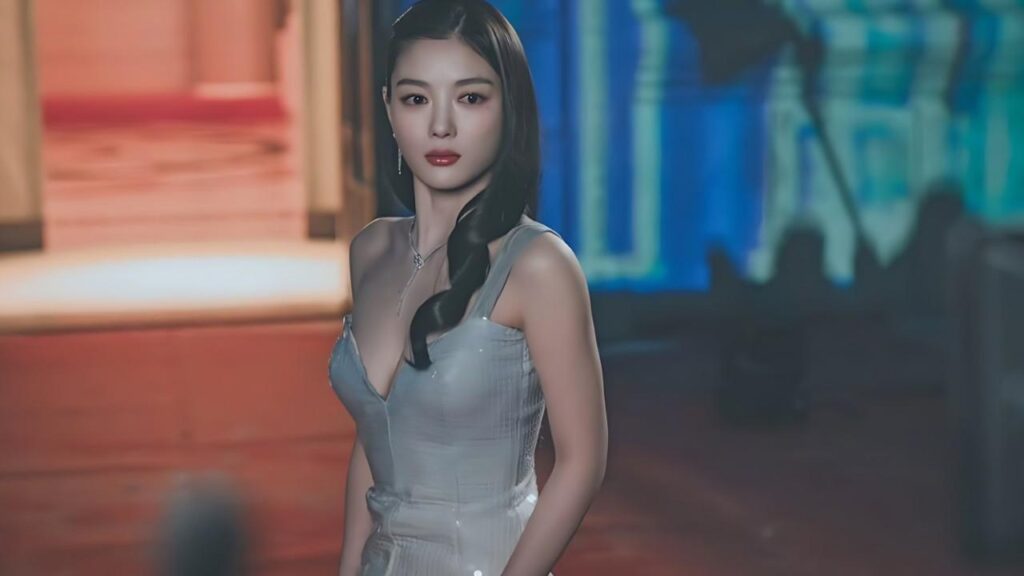 Kim You-jung in a silver, form-fitting dress with a side braid poses before a blurred orange-blue stage.