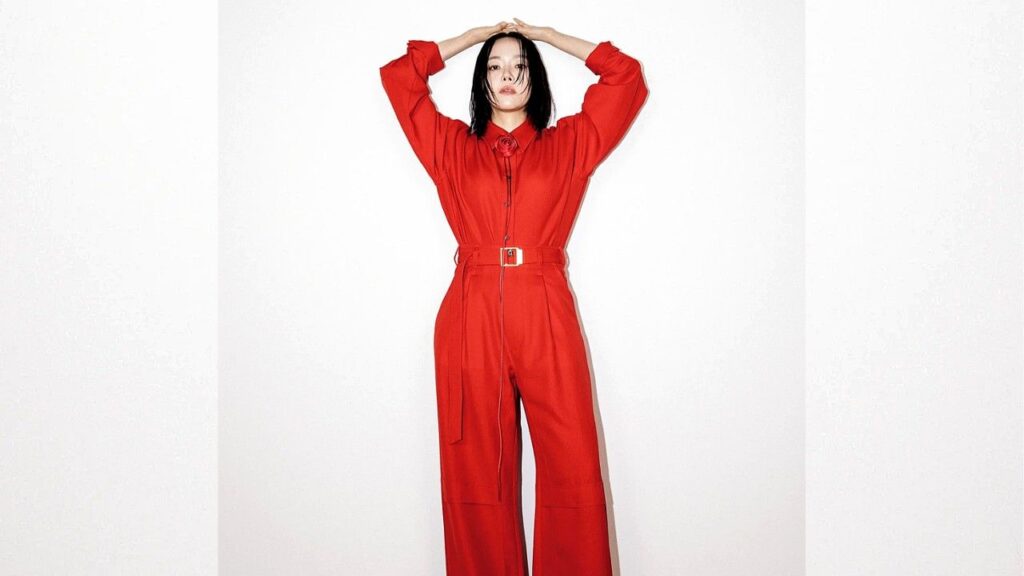 Lee Sang-hee in a vivid red jumpsuit with a belt, arms raised overhead, posing against a plain white studio backdrop.