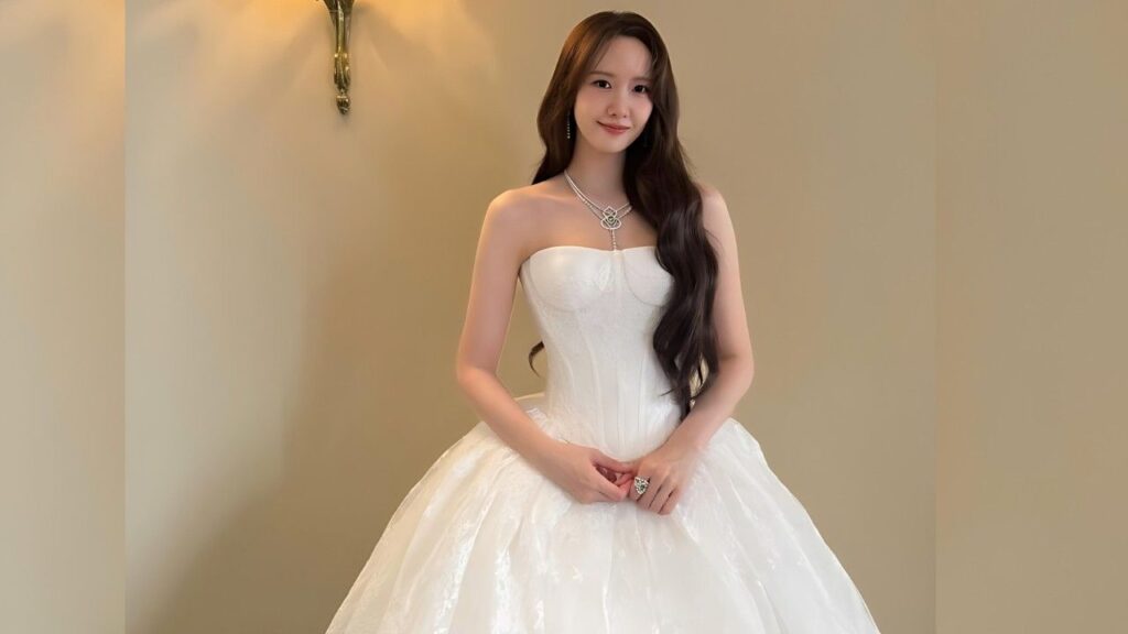 Lim Yoona in a strapless white ball gown with a full skirt and long dark hair, standing, wearing a silver necklace.