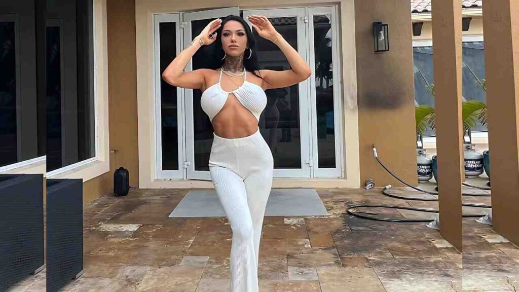 MJ Fresh in a white cut-out halter top and ribbed pants poses on a stone patio, shielding her eyes with raised hands.