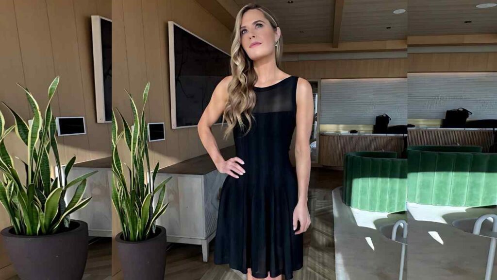 Maggie Lawson in a black dress stands with one hand on her hip in a modern lounge with green velvet seating and snake plants.