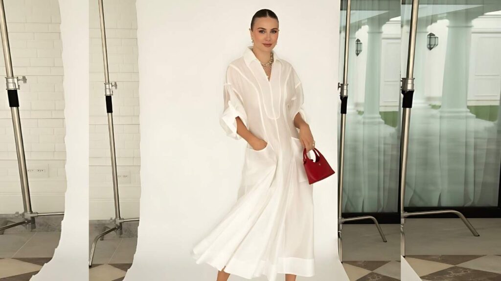 Marthina Brandt in a white shirt dress with rolled sleeves and pockets poses with a red handbag in a bright studio with white backdrops.