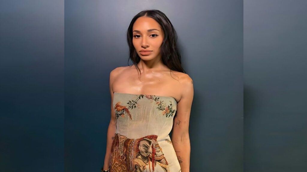 Meaghan Rath with vintage print, a poised woman stands before a blue gradient backdrop, calm expression.