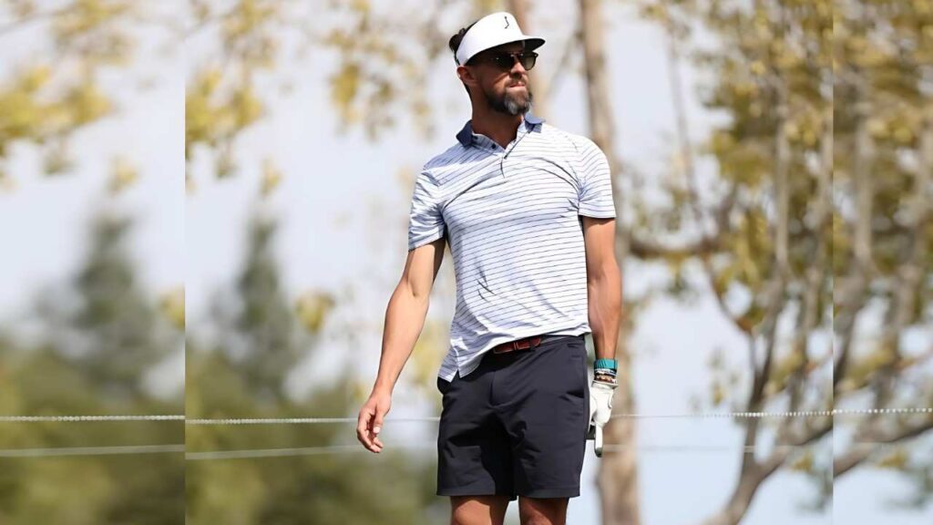 Michael Phelps a sunny course, wearing a white cap, sunglasses, and a light striped polo with dark shorts, gazing to the side.