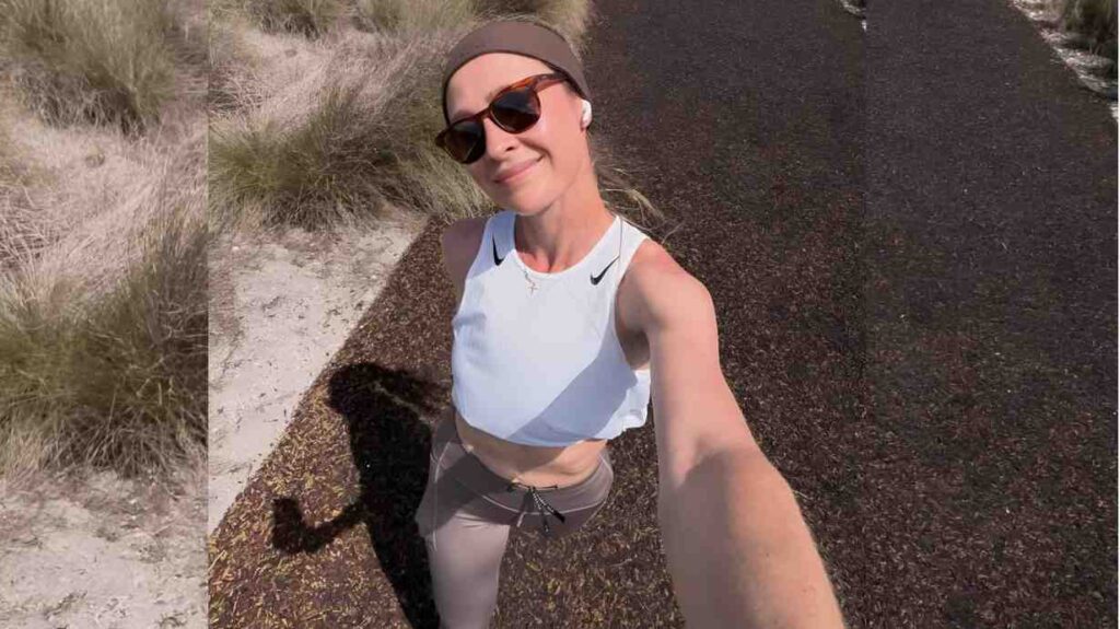 Nelly Korda in a light blue crop top and gray leggings takes a selfie on a desert road, wearing sunglasses and a headband.