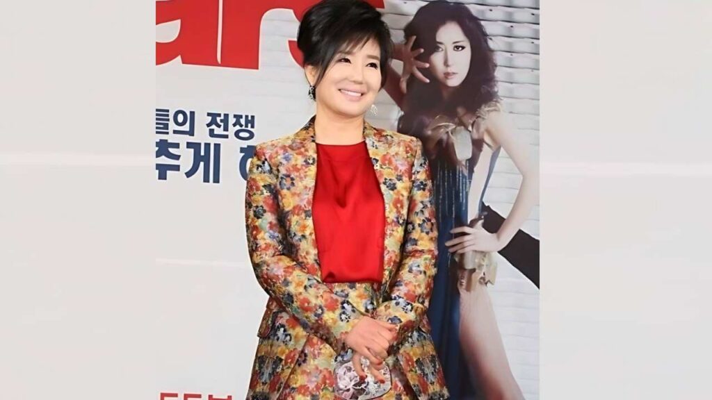 Oh Mi-hee (오미희) in a bright floral blazer and red top, hands folded, posing before a poster with a model and bold Korean text.