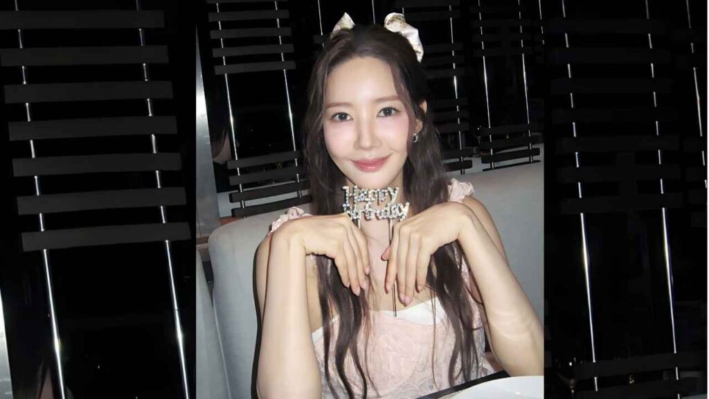 Park Min-young with long dark hair in pink lace top, resting her hands under her chin, holding a Happy Birthday sign