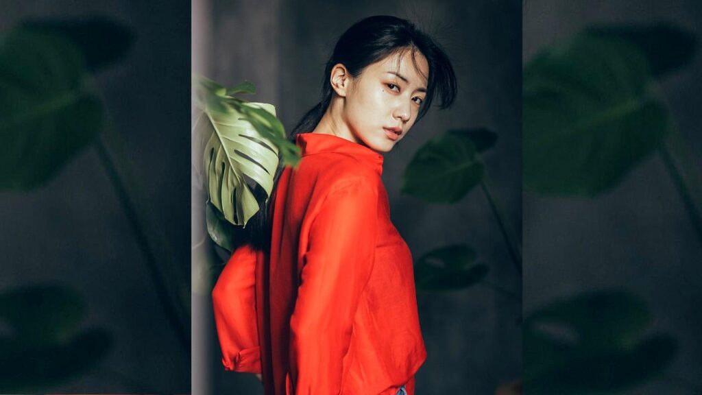 Ryu Hyo-young (류효영) in a vivid red blouse turns toward the camera, with large monstera leaves framing her against a dark backdrop.
