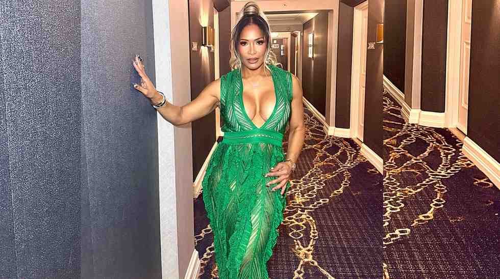 Sheree Whitfield in a bright green plunging-neckline gown stands in a hotel hallway, one hand on the wall.