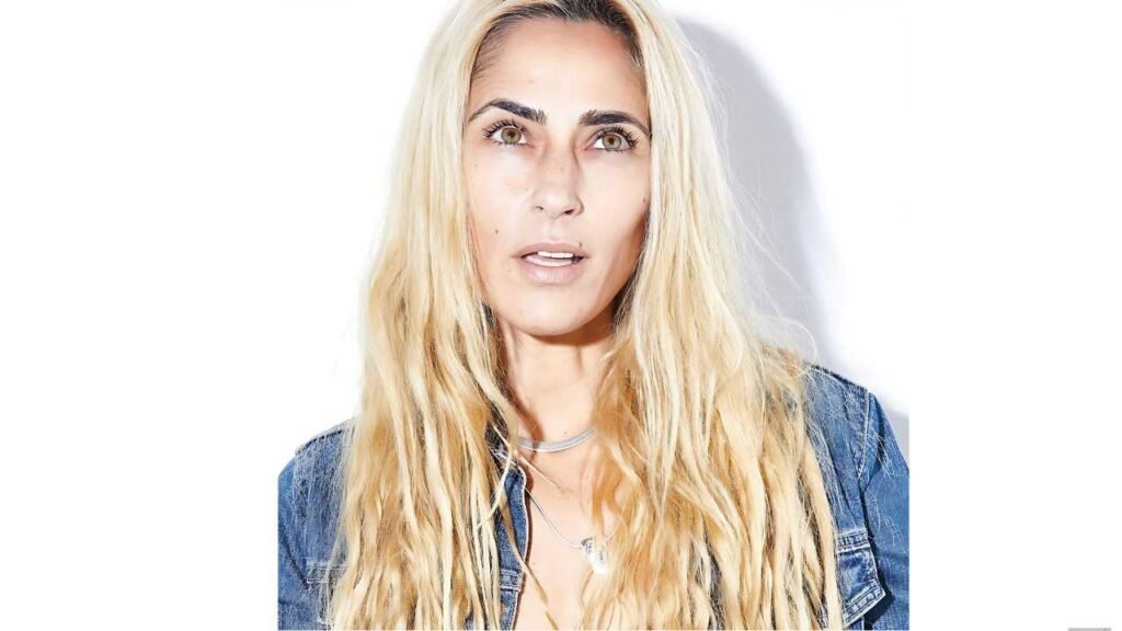 Summer Phoenix with long, wavy hair in a denim jacket, wearing silver necklaces, gazing upward with a thoughtful expression