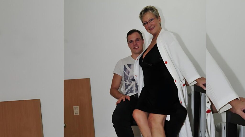 Angelika Jakubowska in a black dress with a white cardigan leaning on the railing beside a man in a graphic tee.
