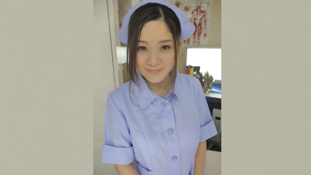 Anna Kimijima in a light blue nurse uniform and cap, smiling at the camera in a clinical room with anatomy posters in background.