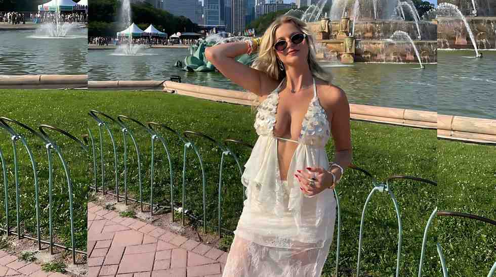 Becky B in a sheer white halter dress and sunglasses poses by a park fountain, holding a pink drink.
