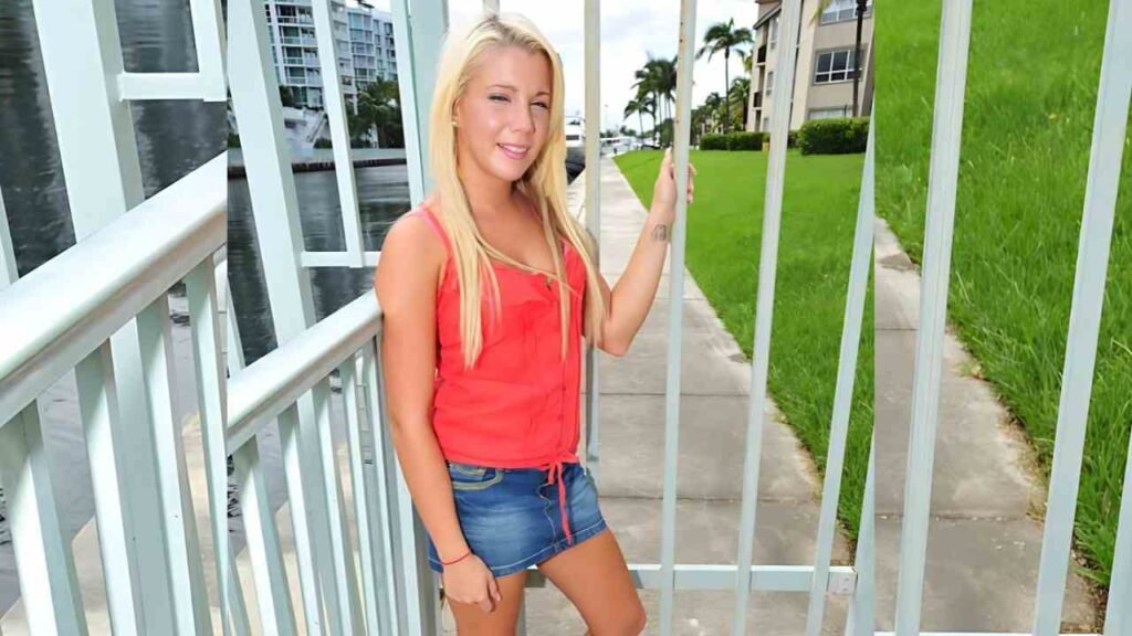 Eva Cole wearing a red top and denim shorts stands smiling outdoors