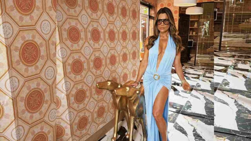 Flavia Alessandra in a blue dress stands beside a gold statue, showcasing a blend of elegance and artistry.