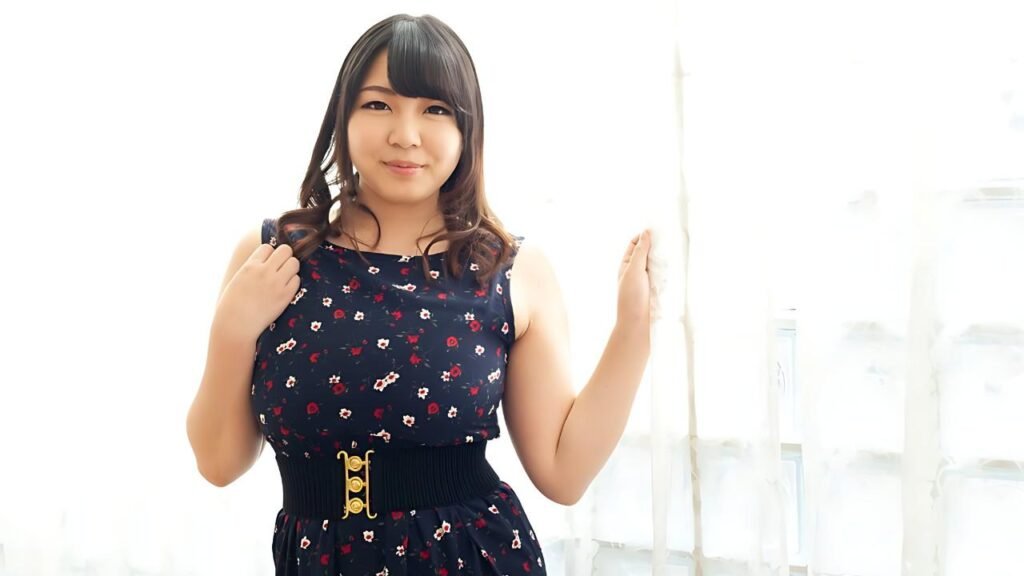 Hikari Minazumi with dark hair and bangs stands by sheer curtains, wearing navy floral dress with a wide black belt, smiling.