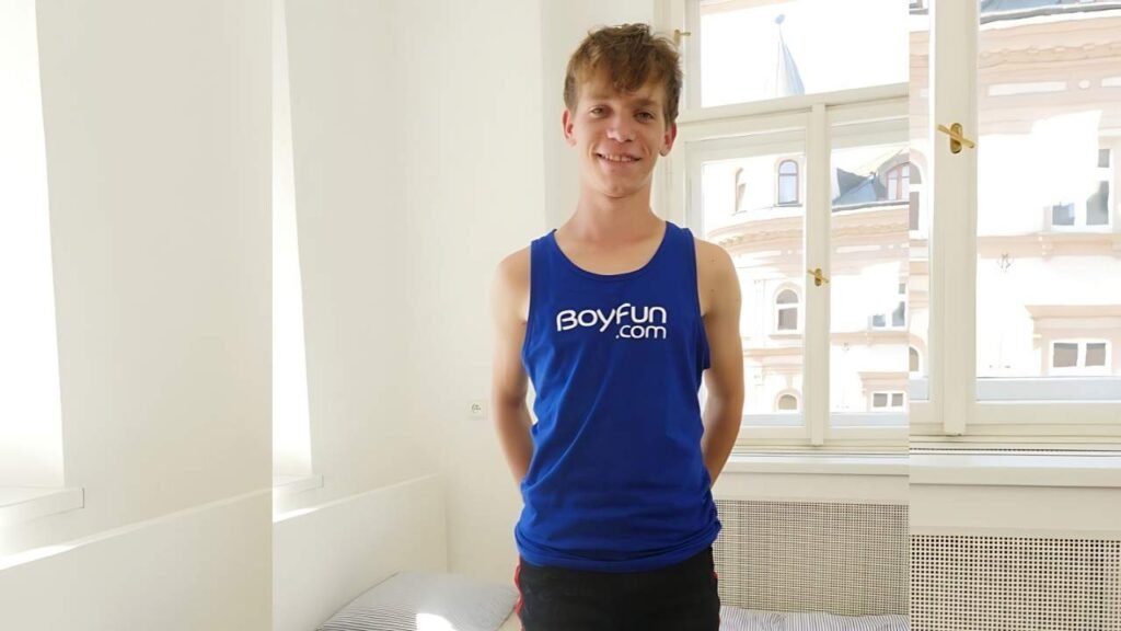 Jacob Dolce in a royal blue sleeveless shirt stands with hands behind his back in a bright white room with large windows.