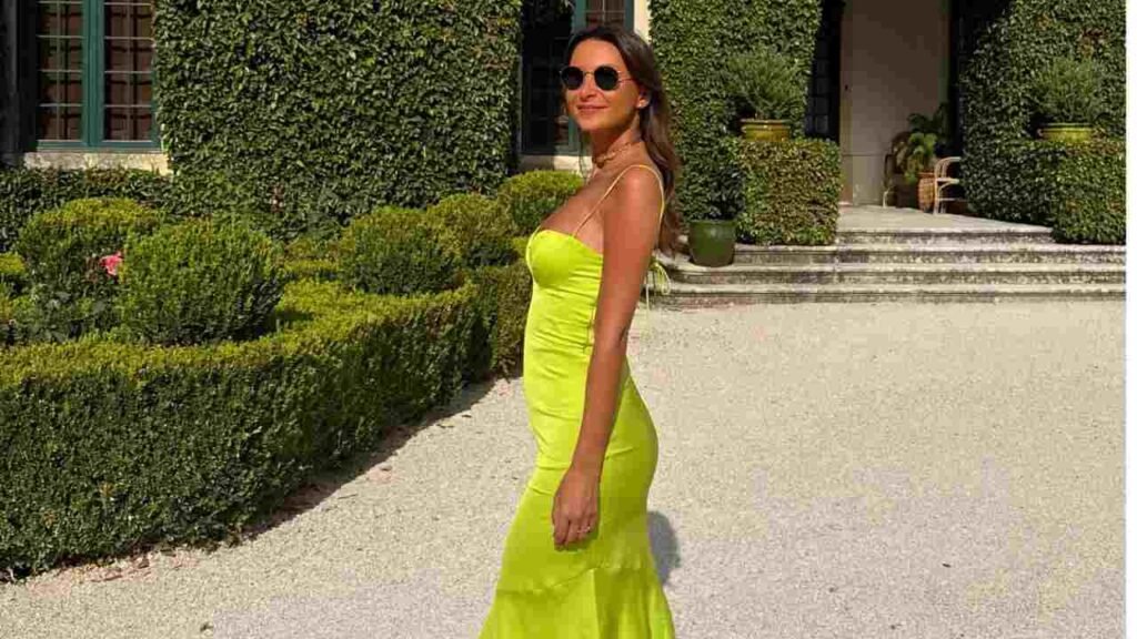 Maria Santos in a neon lime dress with sunglasses, strolling along a gravel path beside manicured hedges and stone steps.