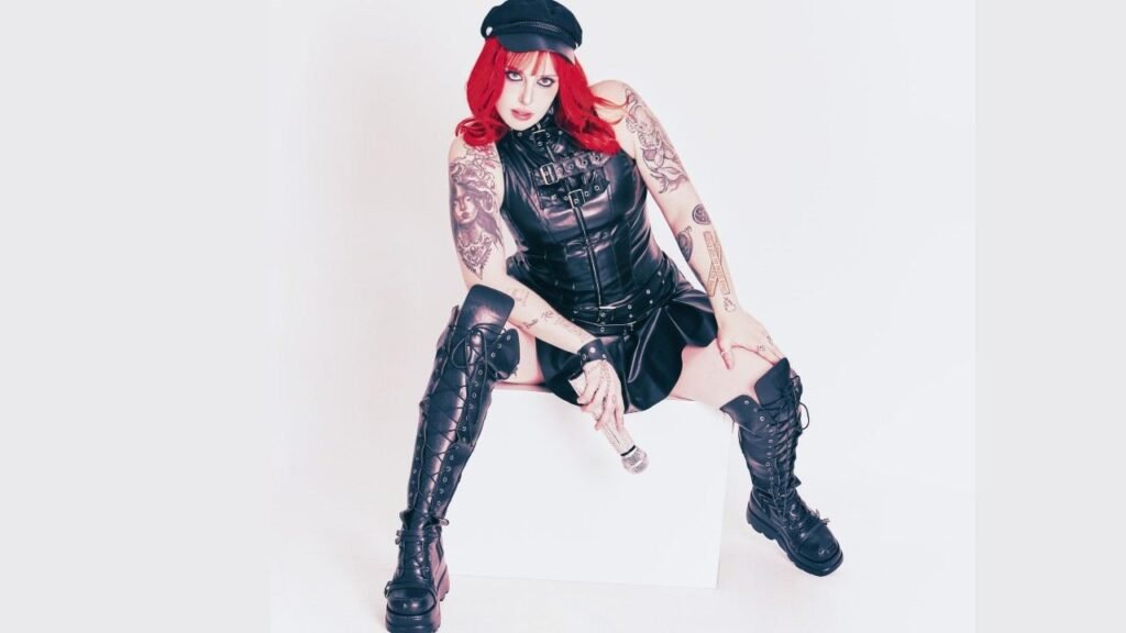 Mel Fire with tattoos and a hat sits on a wooden box, looking thoughtfully into the distance.