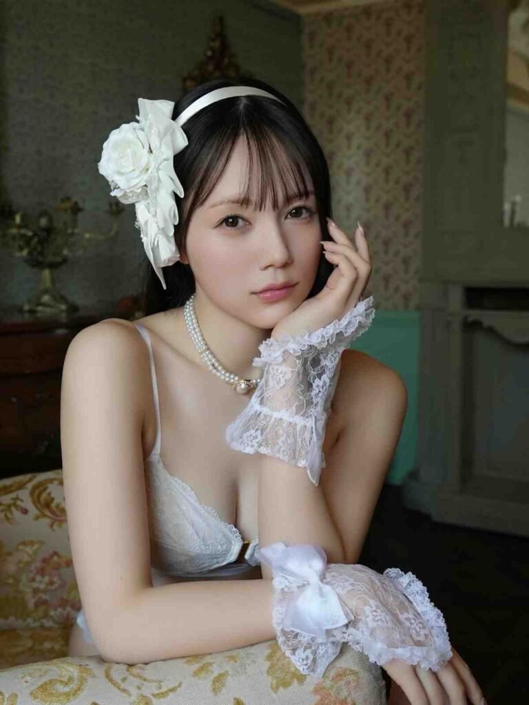 Remu Suzumori in white and gloves, with a large white flower headband and pearl necklace, rests her chin on her hand.