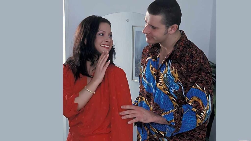 Smiling woman in a red blouse leans into a Robert Rosenberg wearing a dragon-pattern shirt; he rests his hand on her arm in a doorway.