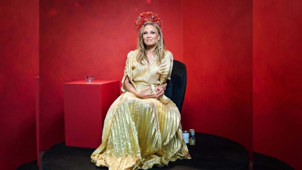 Vanessa Williams wearing a gold dress sits elegantly on a chair, exuding grace and sophistication.