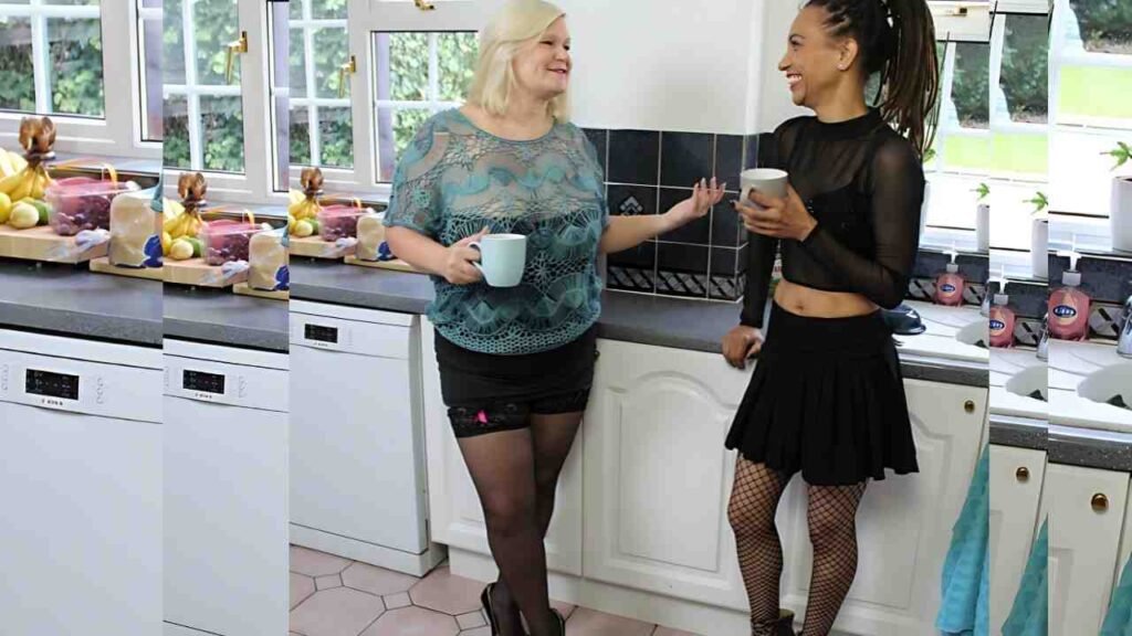 Violette Love chat in a kitchen, mugs in hand; one blonde in teal top and black shorts, the other in a black top and skirt.