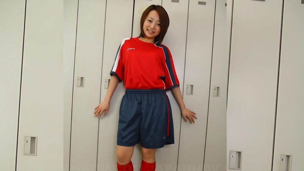 Yu Shiraishi in a red jersey and blue shorts with knee-high red socks leans against a row of grey lockers in a locker room.