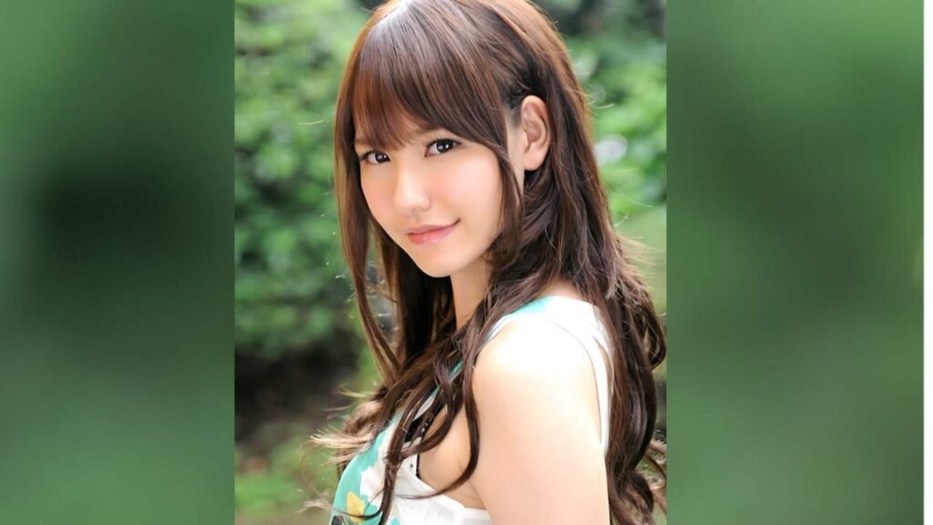 Yui Uehara with brown hair and bangs smiles softly in a sunlit garden, wearing a white sleeveless top with turquoise trim.