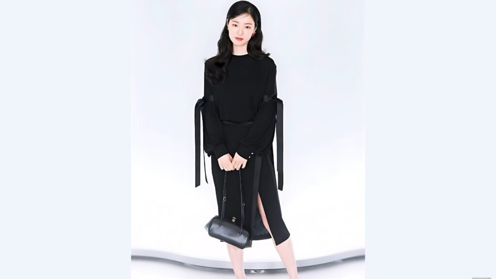 Jeon Yeo-been in a black midi dress with ribboned sleeves and leg slit, hands folded, carrying a purse, against pale backdrop.