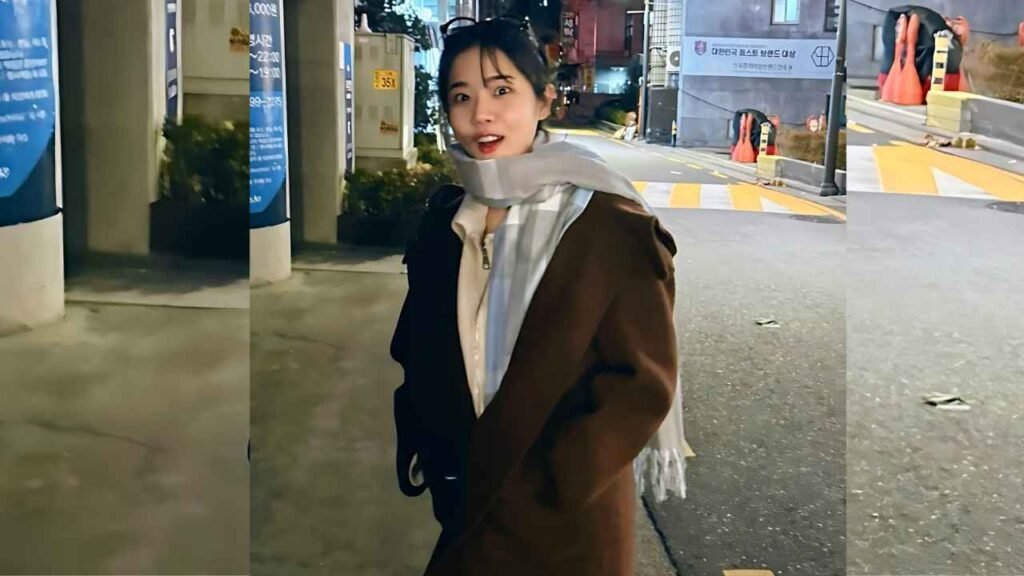 Kim Hyang-gi in a brown coat and white scarf stands on a night street with crosswalk lines and construction barriers behind.