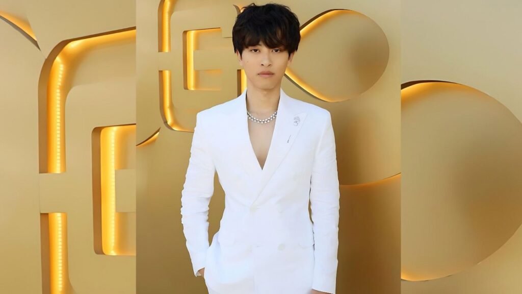 Alan Chikin Chow dressed in a white suit and tie poses against a luxurious gold wall backdrop.