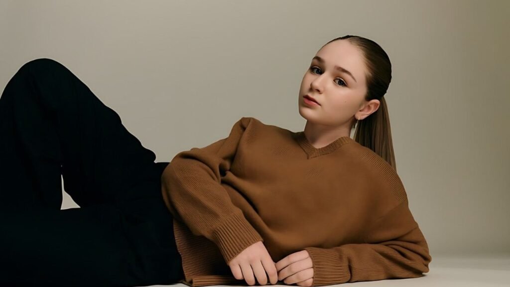 Alix West Lefler in a brown sweater is lying on the floor, looking relaxed and comfortable.