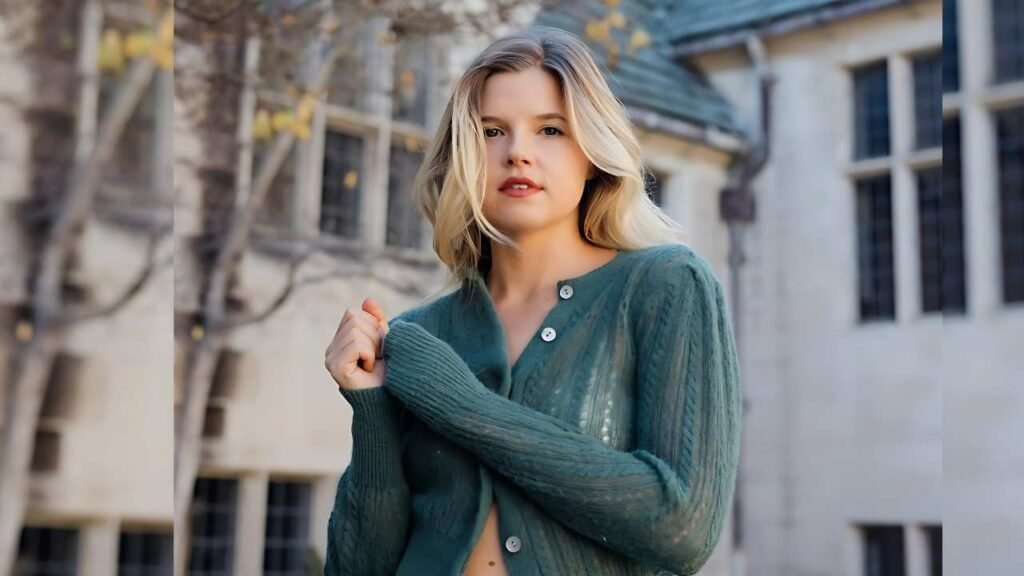 Ana Mulvoy Ten wearing a green sweater smiles while posing for a photo against a neutral background.