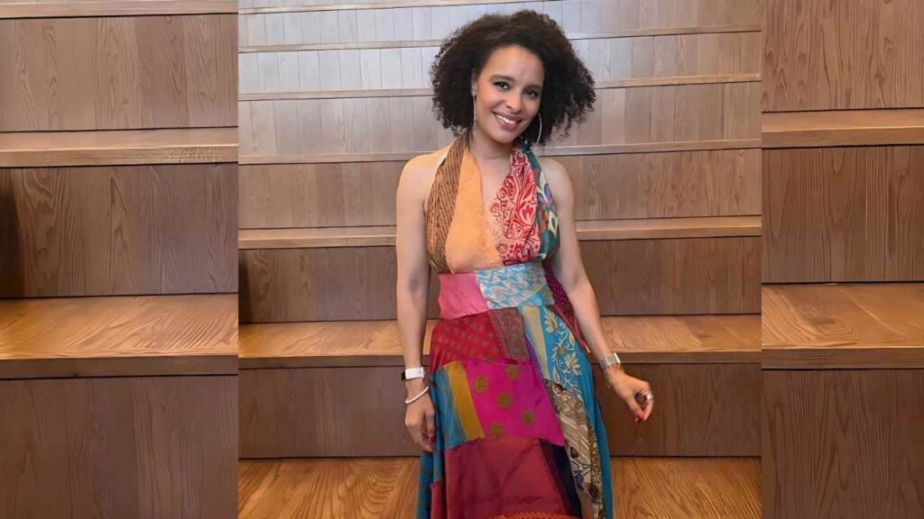 Antonique Smith in a vibrant, colorful dress stands gracefully on a polished wooden floor.