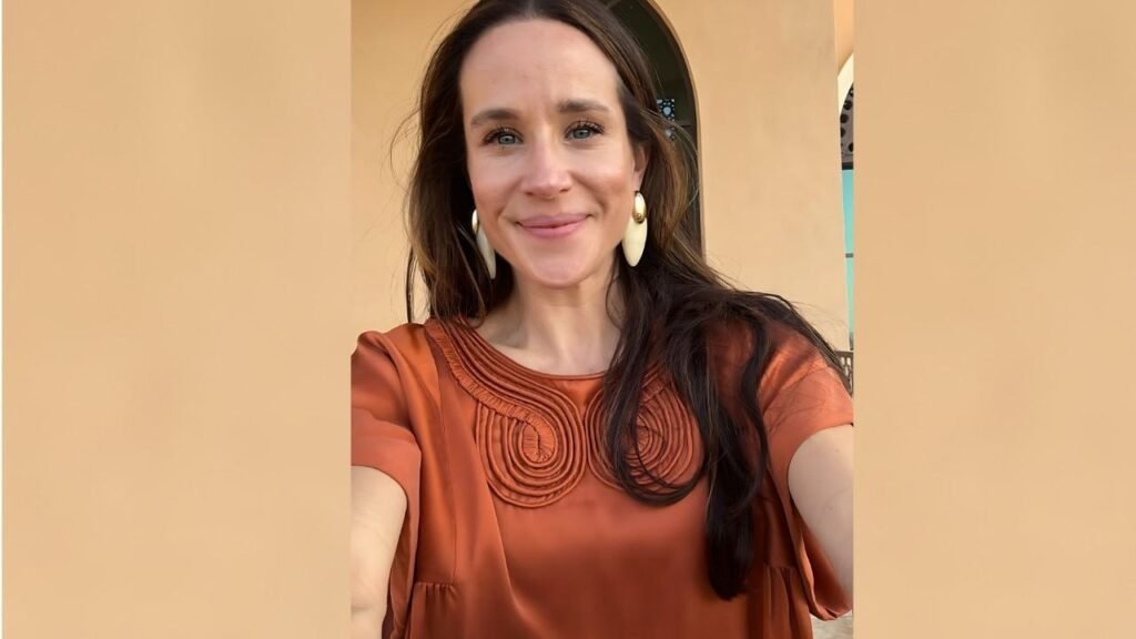 Ashley Biden wearing an orange top smiles warmly at the camera, exuding a cheerful and positive demeanor.