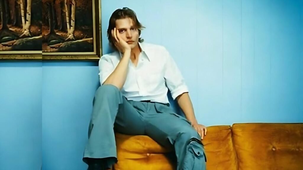 Barry Pepper sits thoughtfully on a couch, resting his chin on his hand, reflecting or pondering an idea.