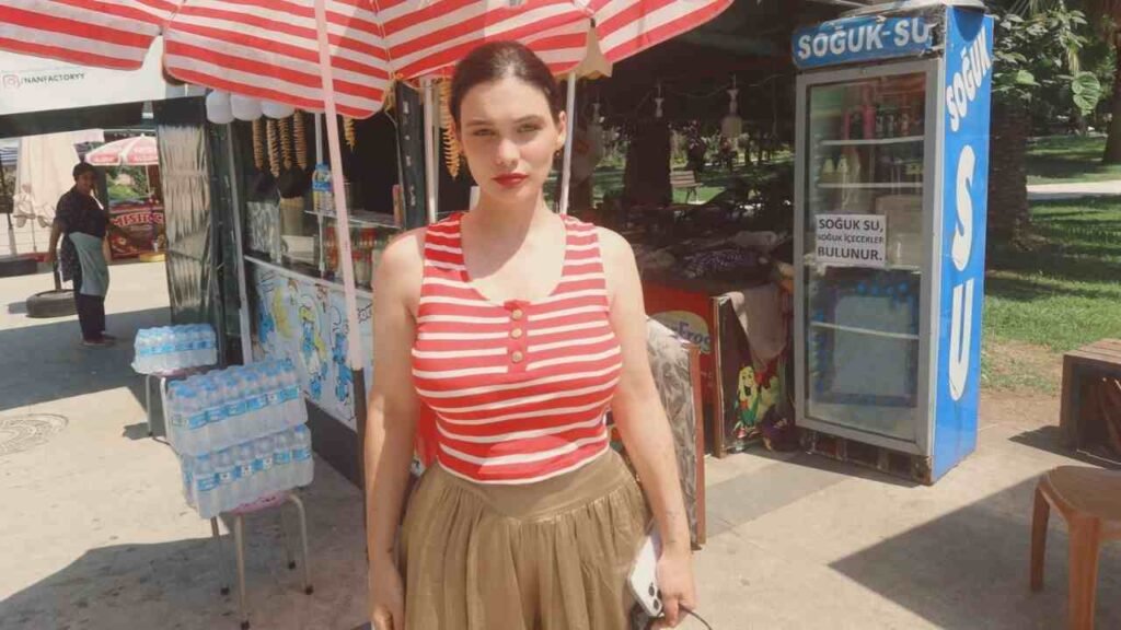 Beste Kokdemir dressed in a striped shirt and brown trousers poses, highlighting her fashionable and relaxed attire.